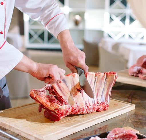 A man cook cuts meat with a knife in a restaurant.