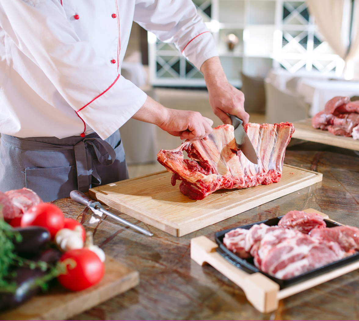 A man cook cuts meat with a knife in a restaurant.