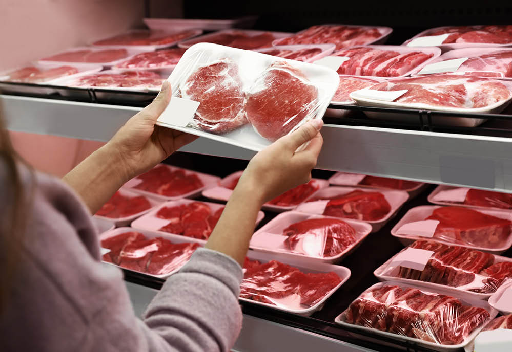 Woman taking packed pork meat from shelf in supermarket